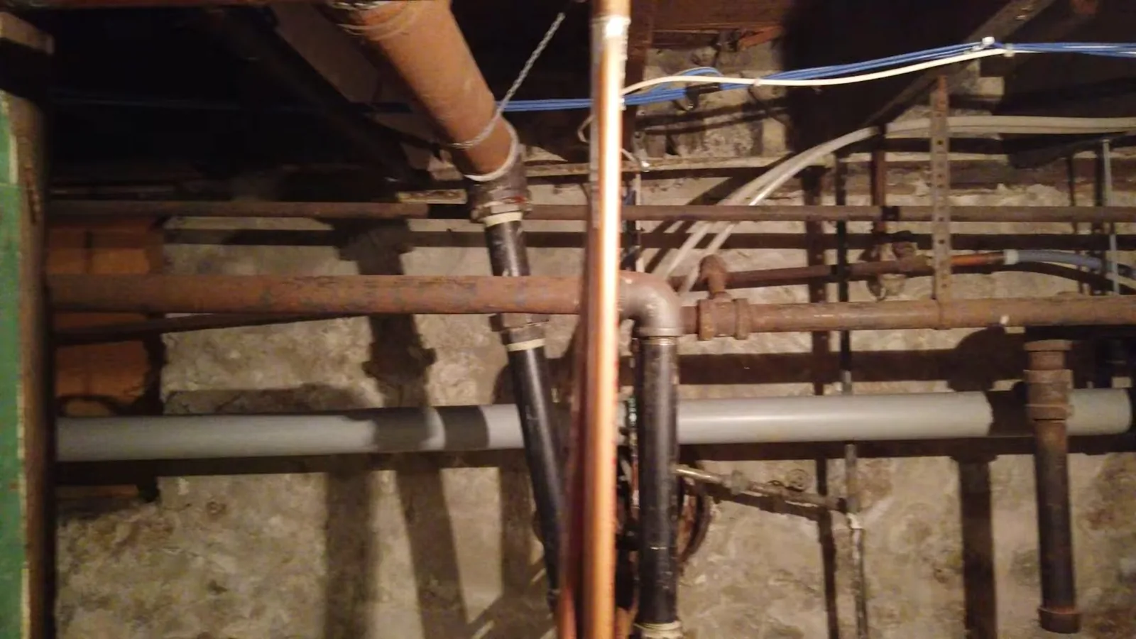 Basement ceiling with copper, iron and plastic pipes running between joists.