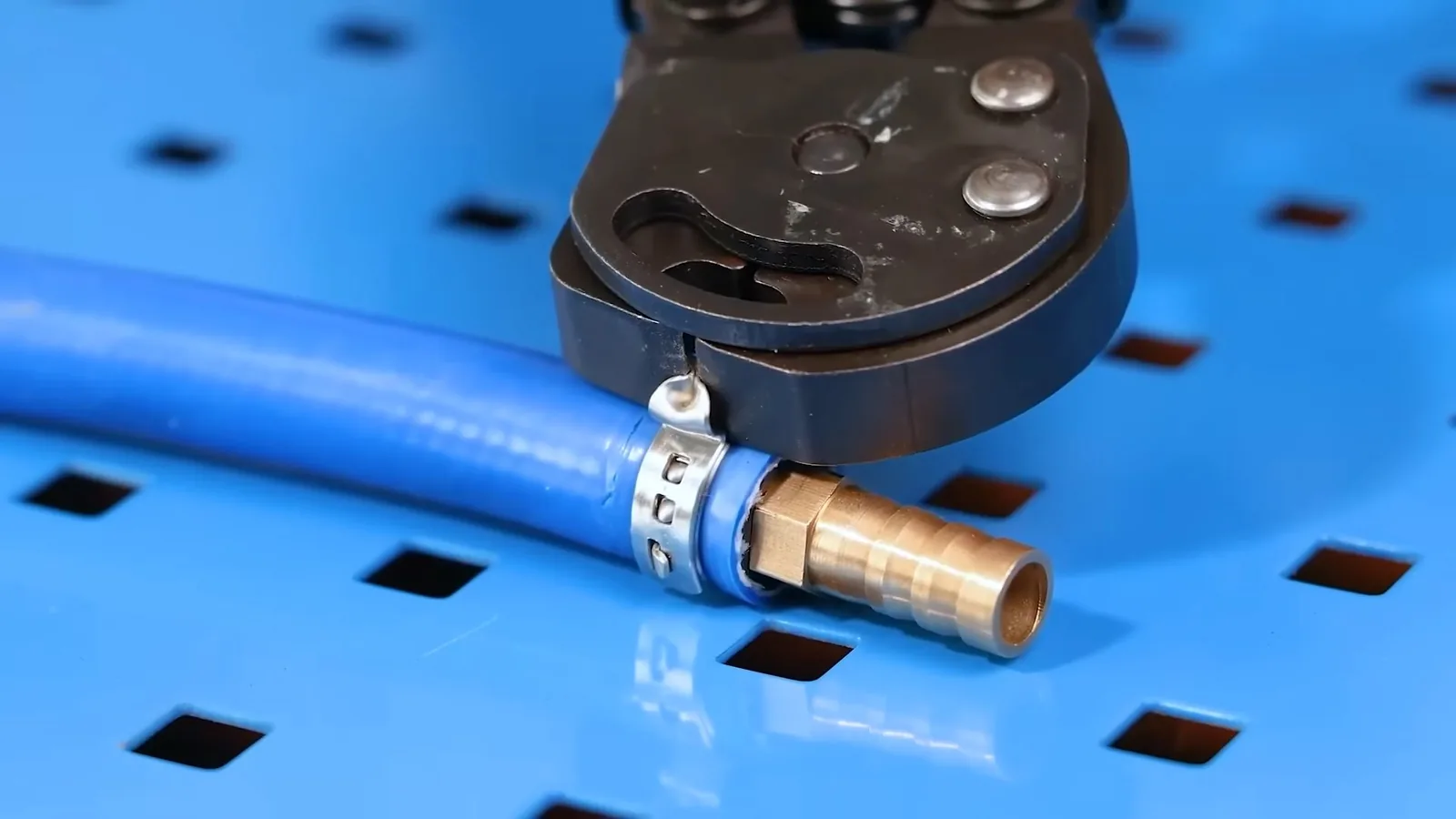 Blue PEX tubing with a crimp ring and brass fitting under a crimping tool on a blue pegboard.