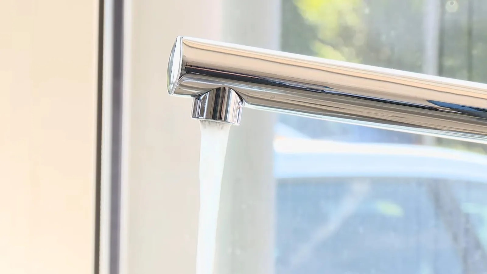 Chrome kitchen faucet running water in front of a window.