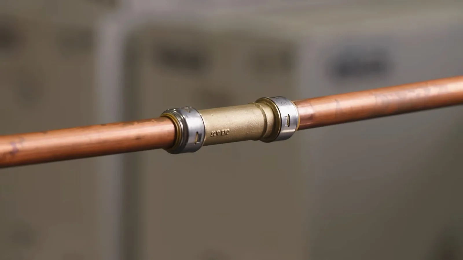 Copper pipe with a metal push-fit coupling joining two sections against a blurred background.