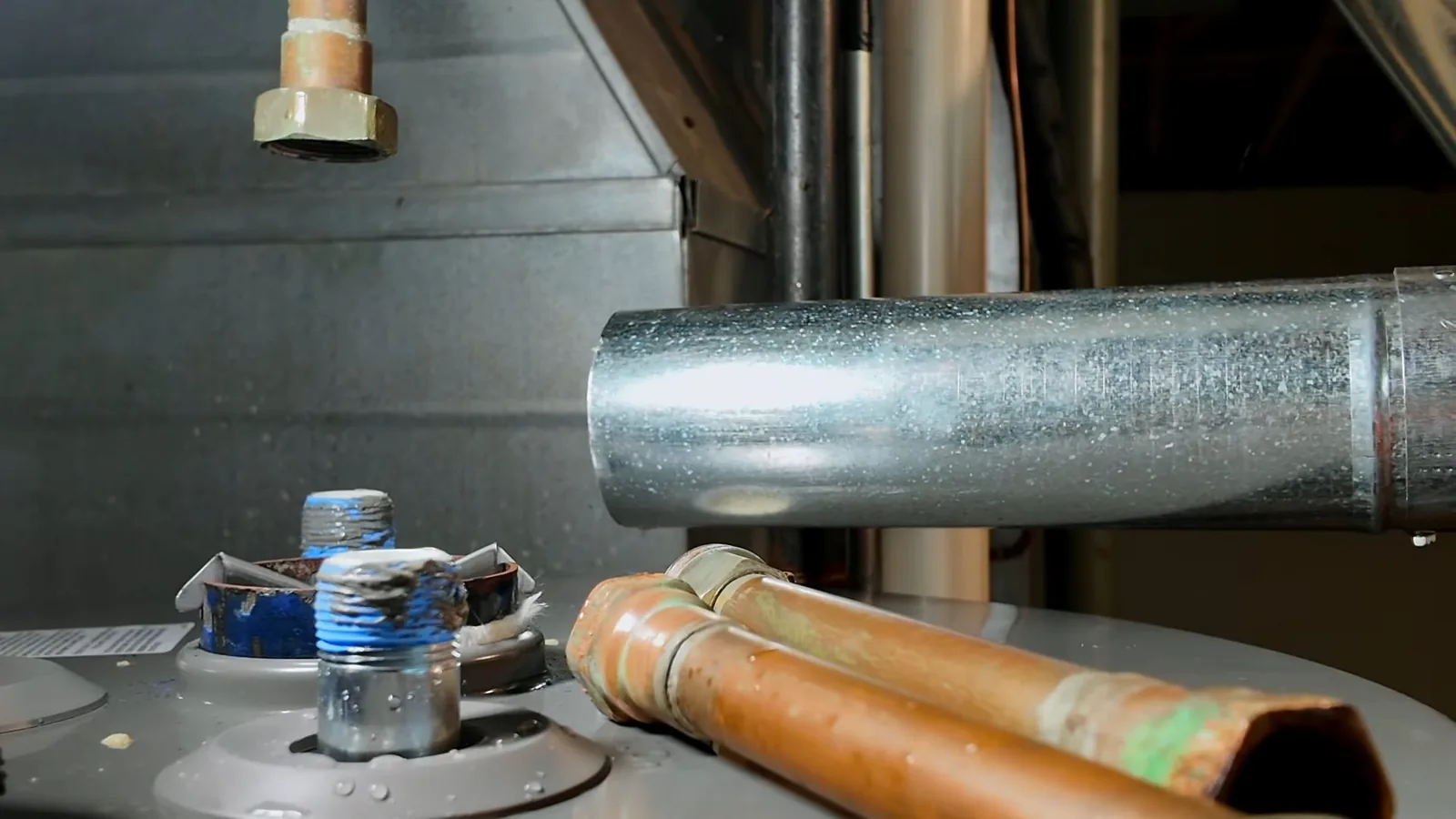 Copper and threaded pipe stubs on top of a water heater beside a galvanized duct.