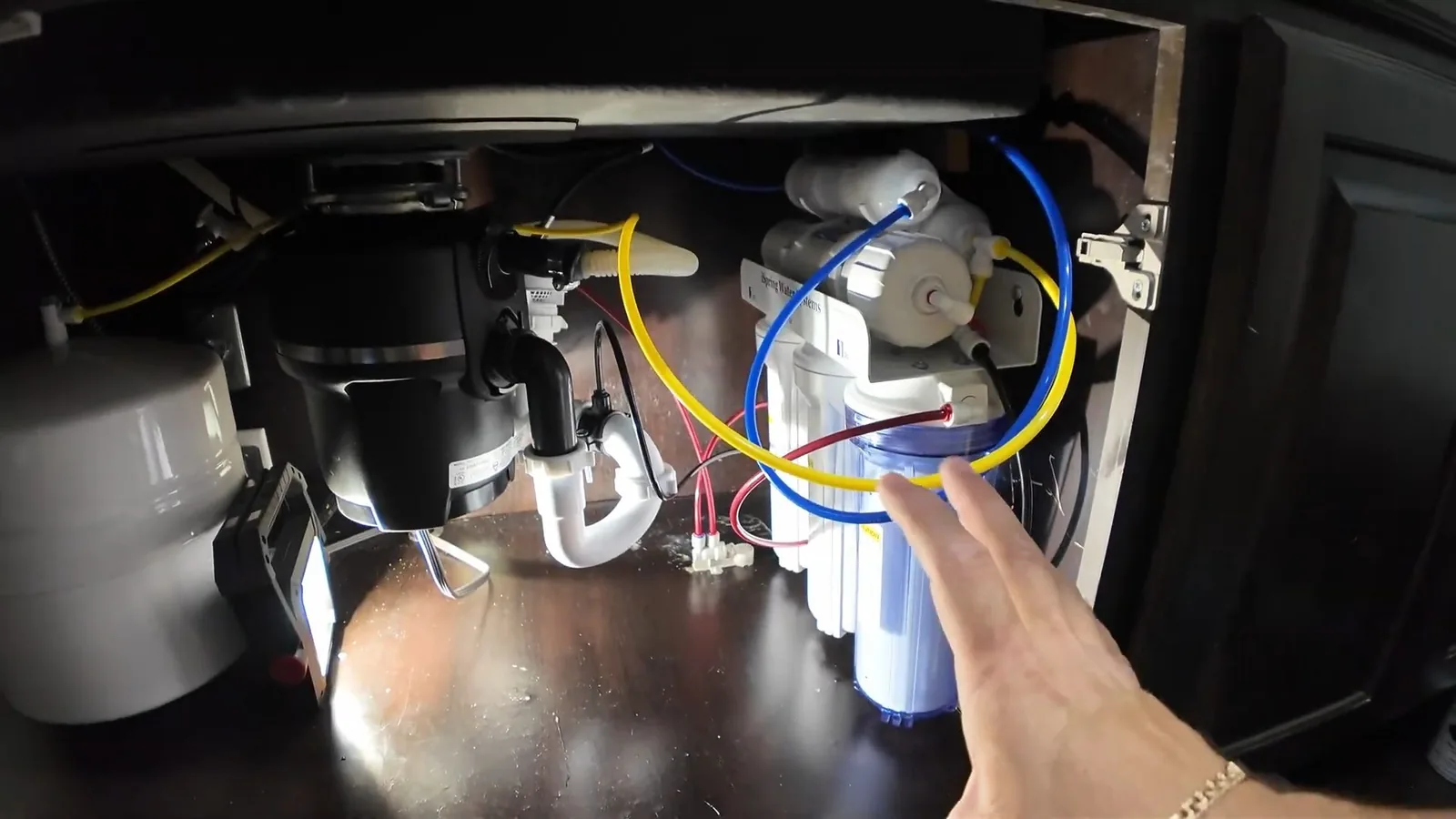 Garbage disposal and a water filter set under a sink, with a hand pointing at the filter housings.