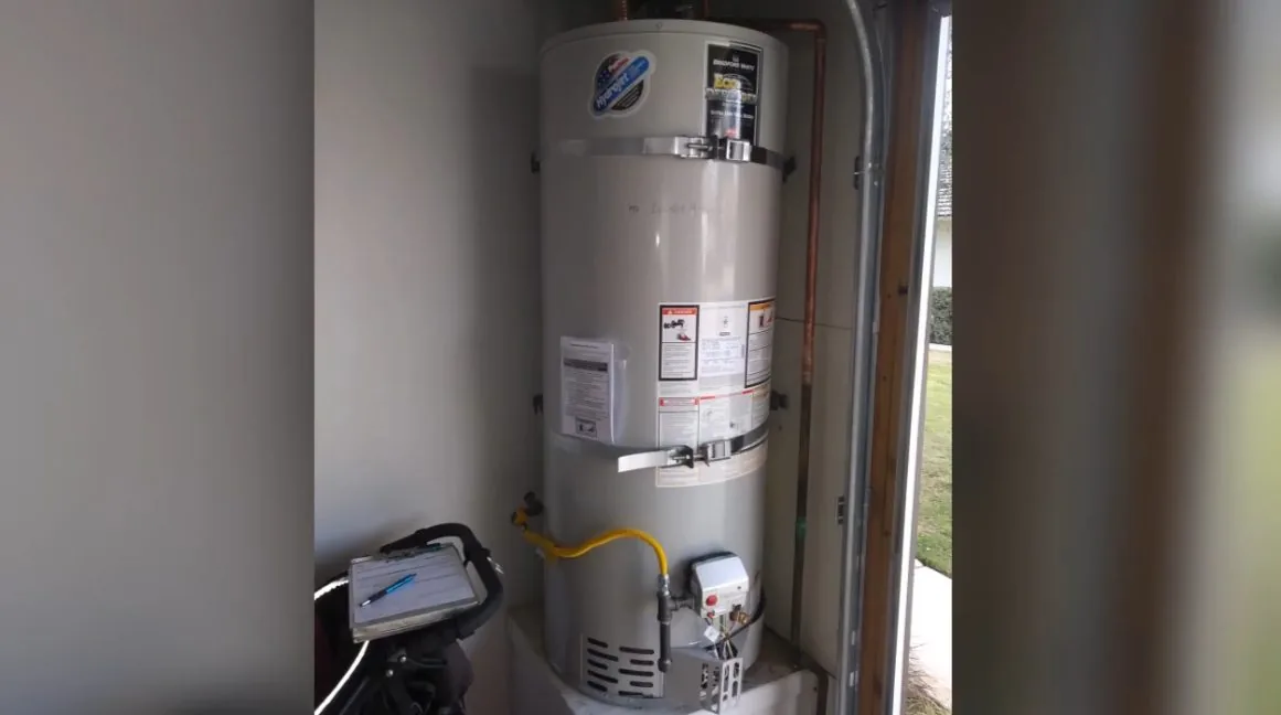 Gas tank water heater standing in a narrow closet with a yellow gas line and a vent connection at the top.