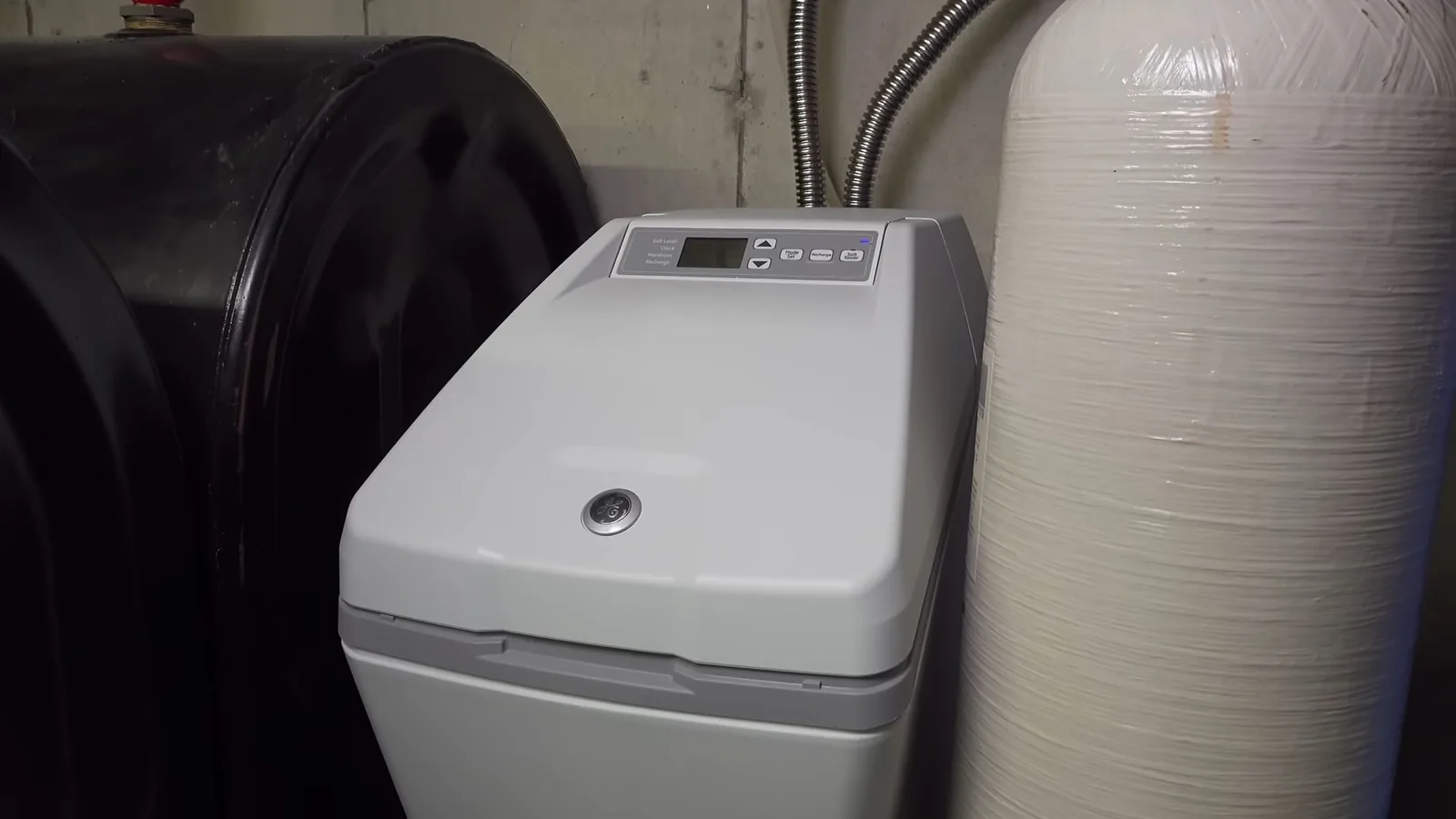 Gray water softener cabinet standing beside a white mineral tank and a black brine tank.