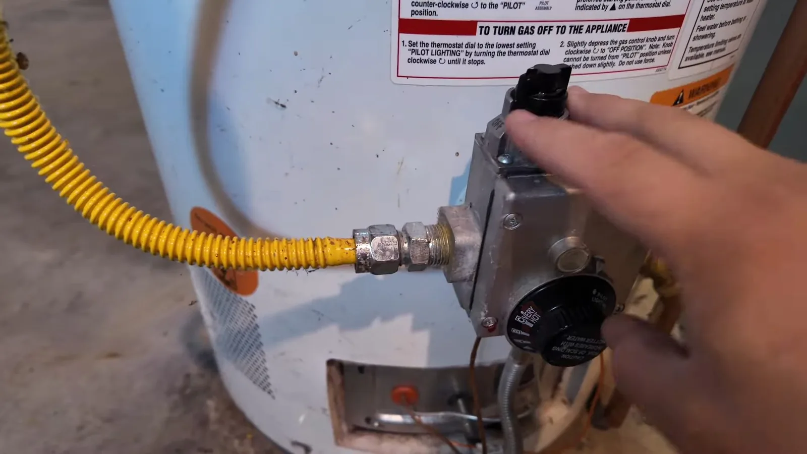 Hand turning the control dial on the gas valve at the base of a tank water heater.