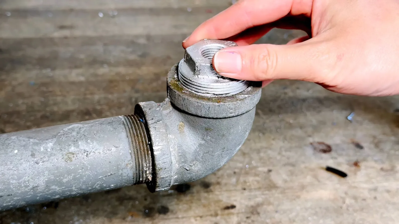 Hand unscrewing the threaded cap of a galvanized cleanout fitting on a concrete floor.