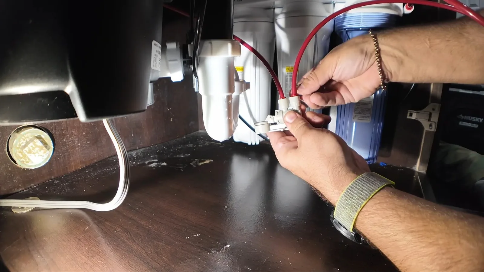 Hands connecting wires beside a garbage disposal under a sink.