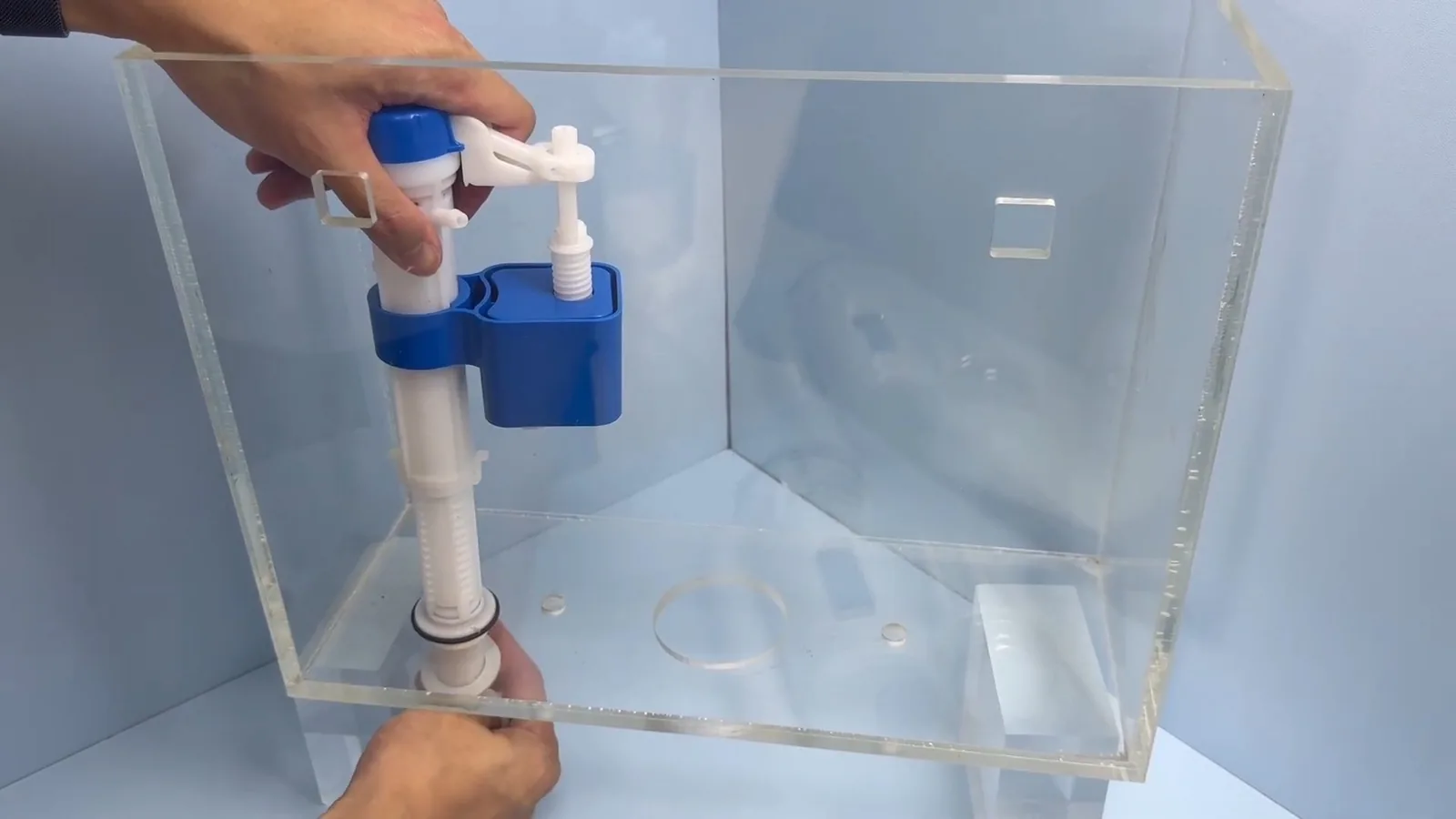 Hands fitting a blue and white fill valve assembly inside a clear toilet tank.