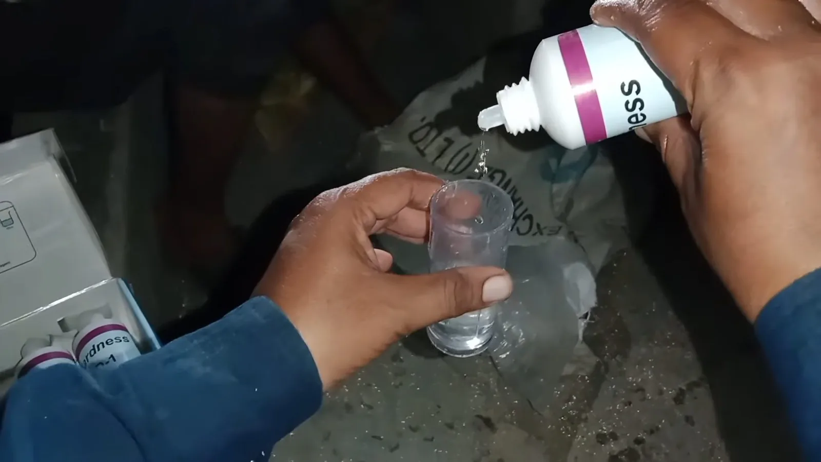 Hands holding a small glass while squeezing drops from a bottle into it, a water hardness test.