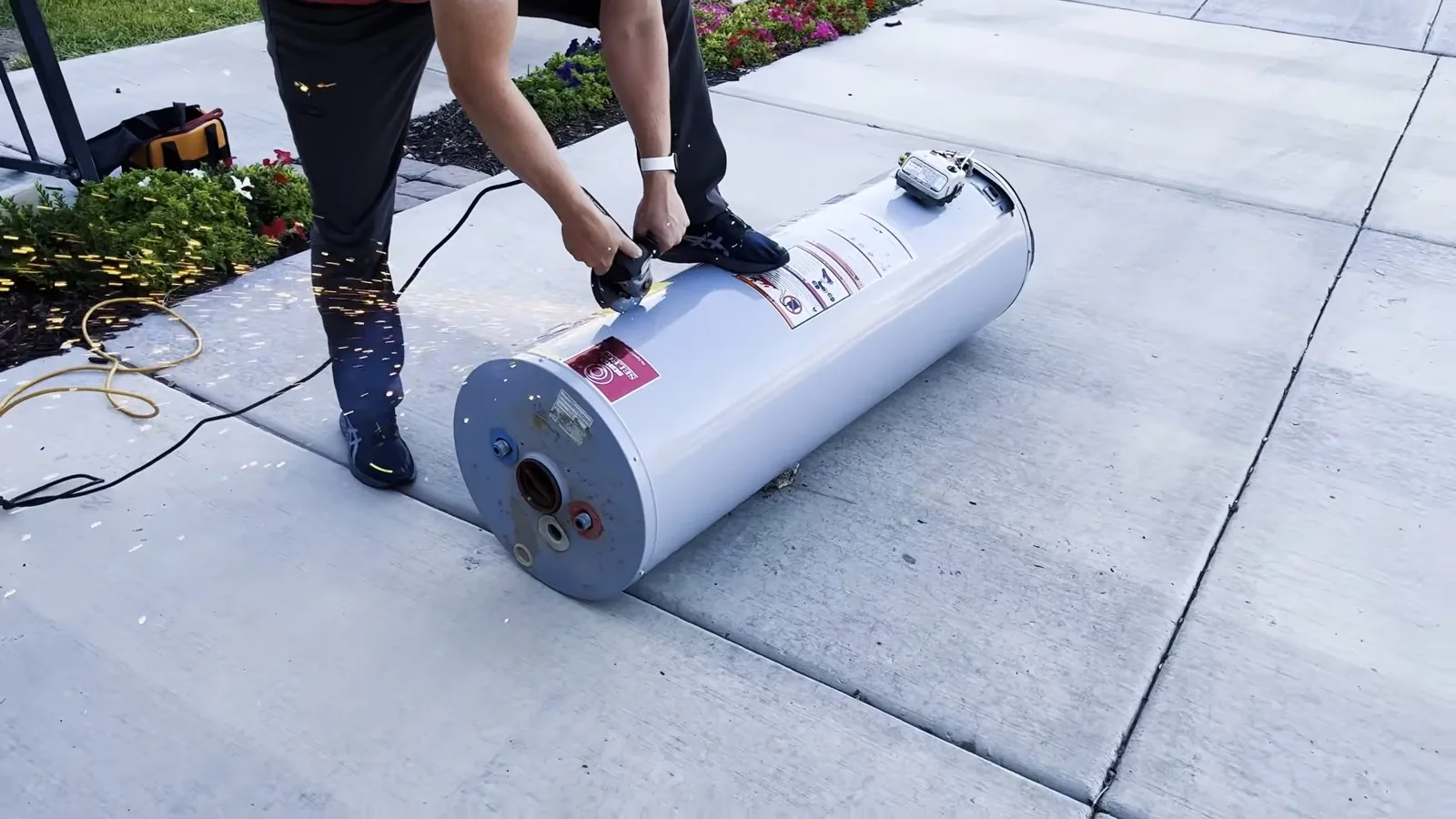 Person bending over a white tank water heater lying on its side on a concrete driveway.