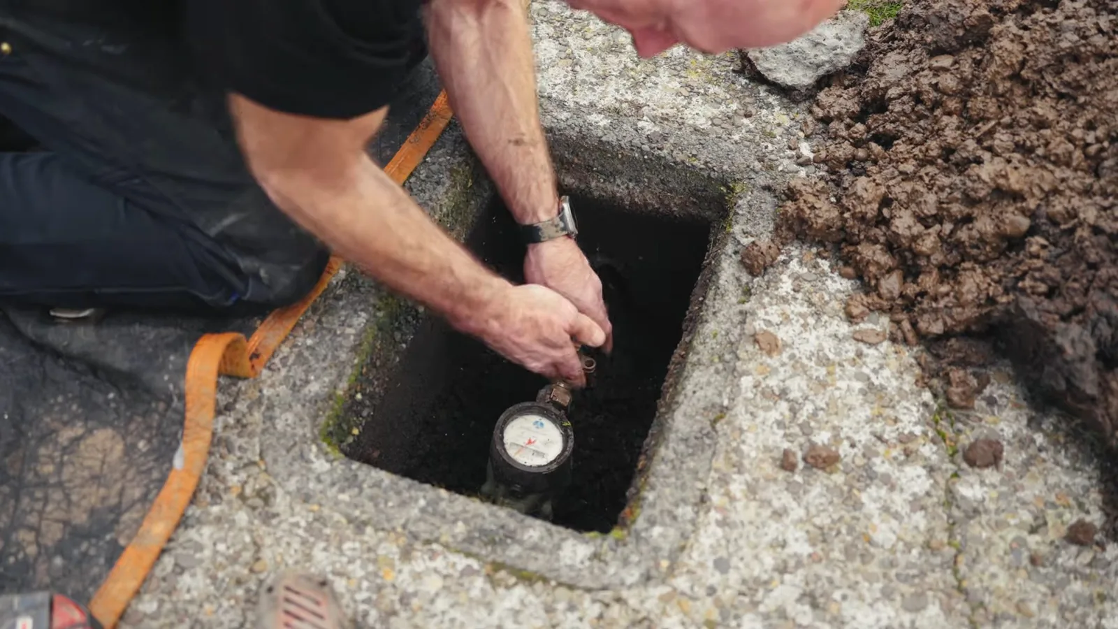 Person reaching into a concrete meter box in the ground to read a water meter.