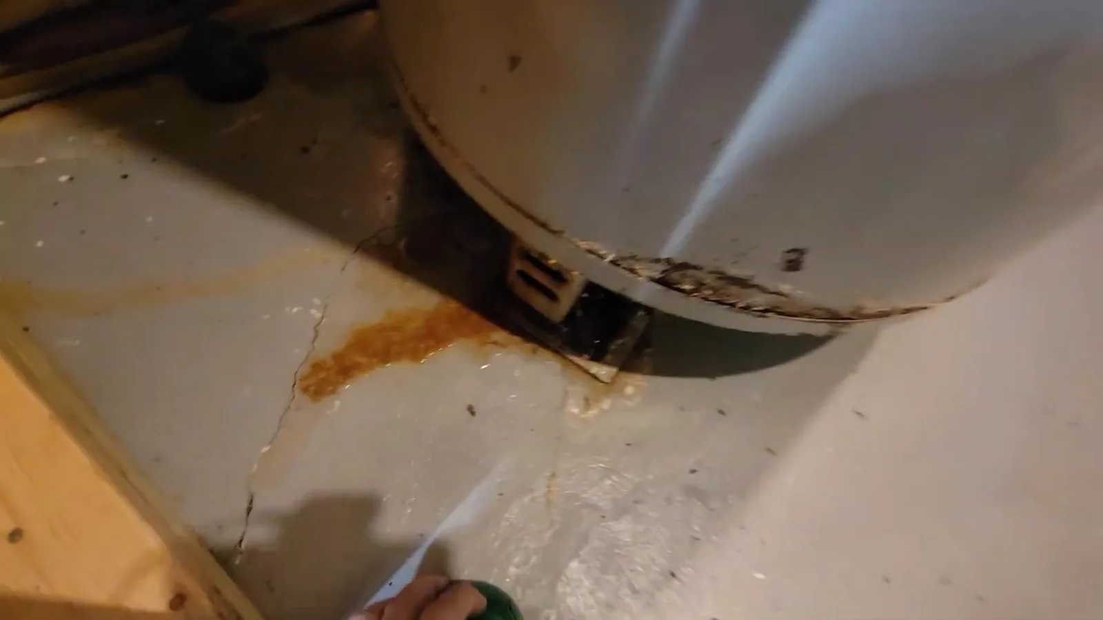Rust-colored stain on a concrete floor beneath the base of a tank water heater.