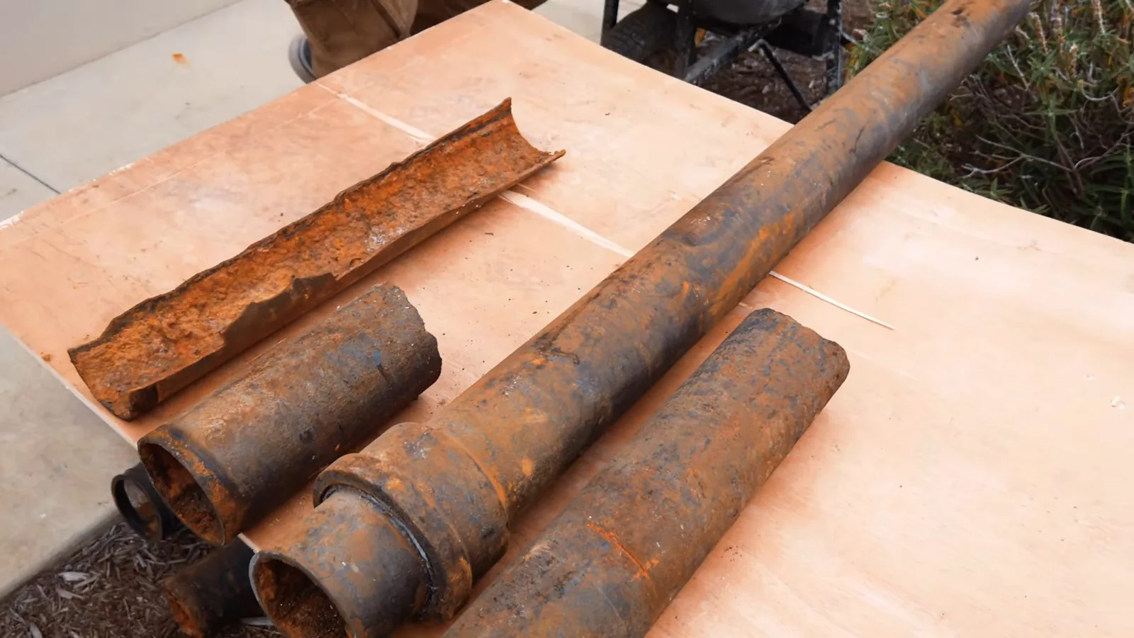 Rusted cast-iron pipe sections laid on a plywood sheet, one split lengthwise.