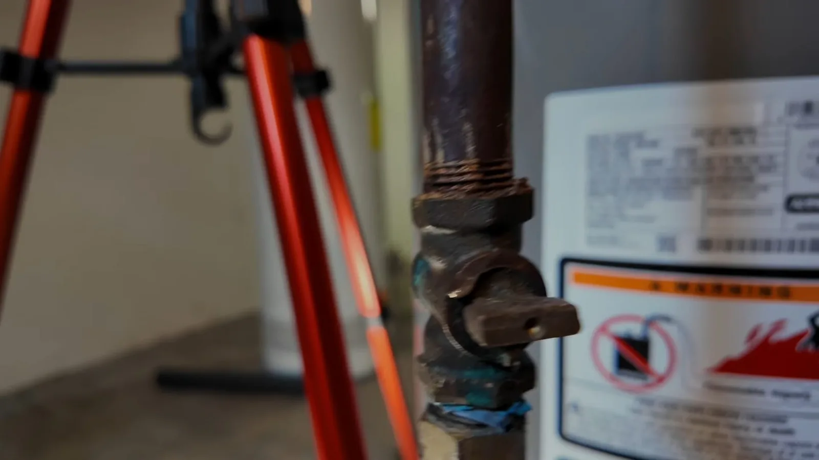 Iron pipe with a lever shutoff valve beside the warning label of a water heater.