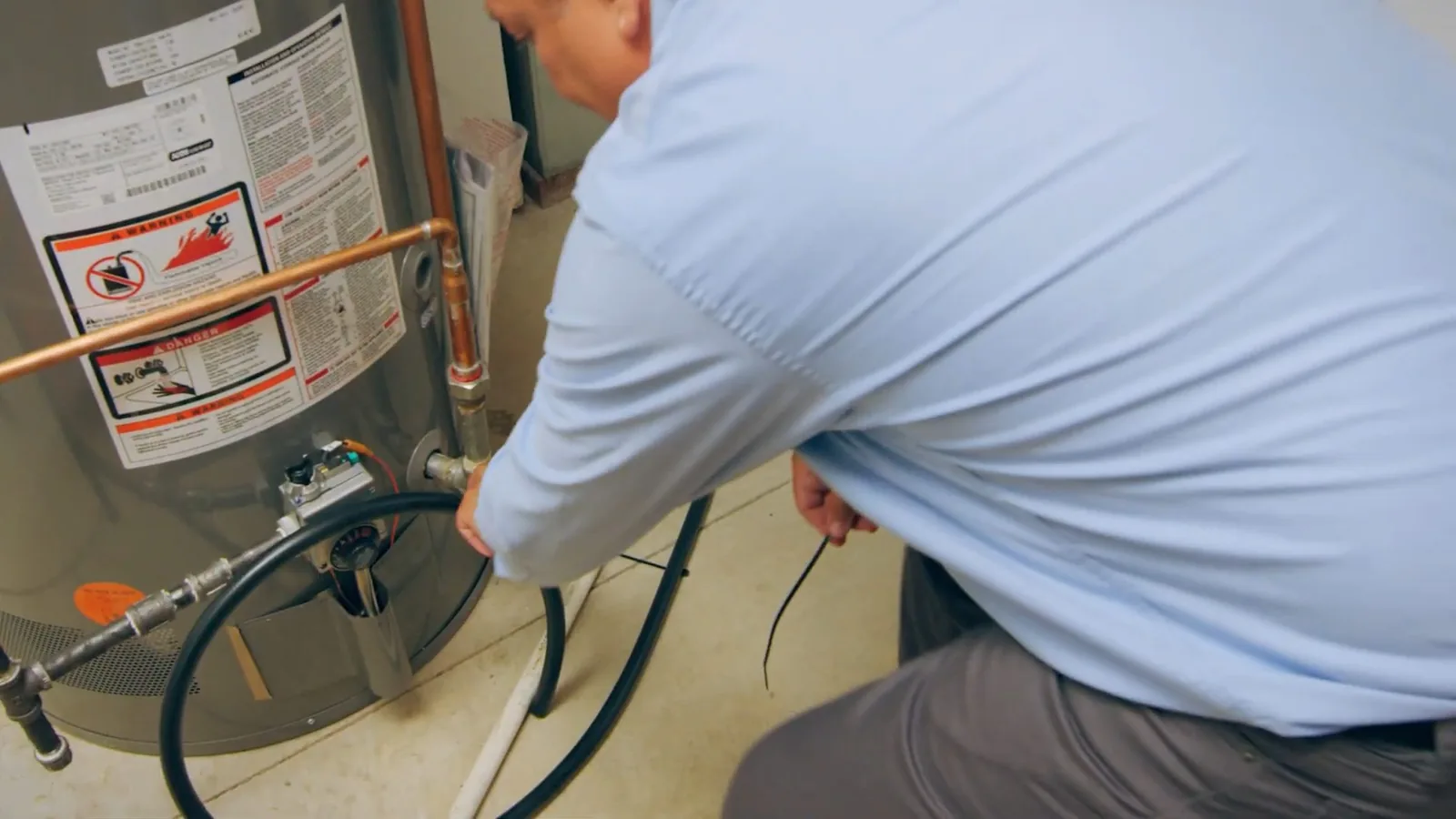 Technician in a light blue shirt working at the fittings on the side of a tank water heater.