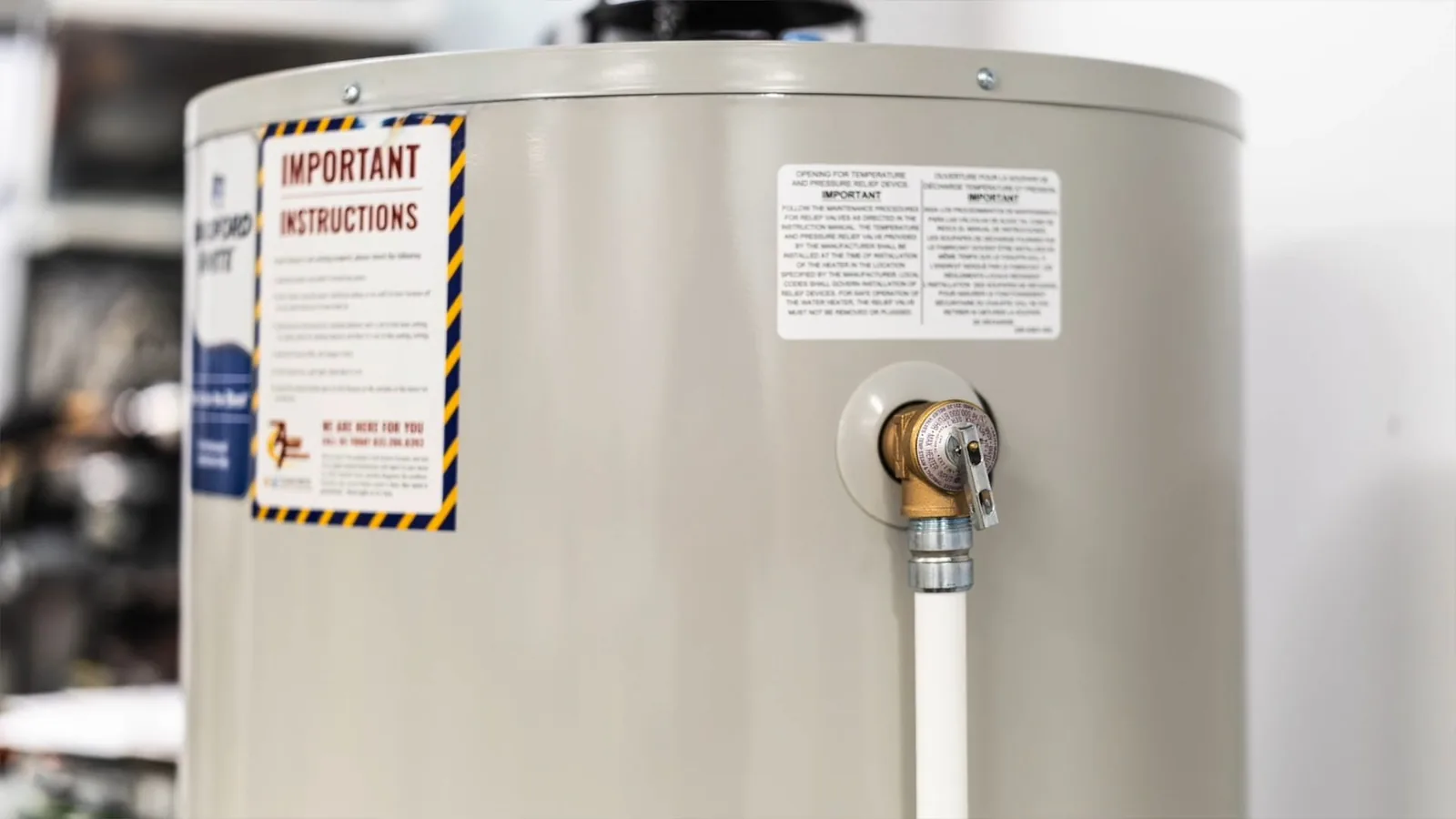 Tank water heater with warning labels and a brass relief valve with a discharge pipe.